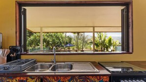 A kitchen with a window view, a sink, a stove, and a colorful backsplash. - Temenino Pihiti Secluded Bungalow (Taiarapu-Ouest)