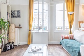 Ein modernes Wohnzimmer mit Sofa, Couchtisch, Bücherregal, Heizkörper und einem Fenster mit Vorhängen.