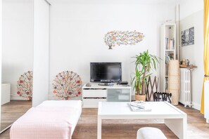 Ein modernes Wohnzimmer mit Flachbildfernseher, Glastisch, Sofa und dekorativer Wandkunst.