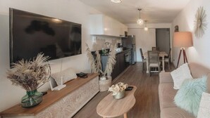 A modern living room with a flat-screen TV, wooden furniture, a dining area, and a kitchen in the background. - Elegance in Barranco - Cozy 2BR (Lima)