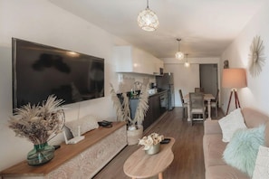 A modern living room with a flat-screen TV, wooden furniture, a dining area, and a kitchen in the background. - Elegance in Barranco - Cozy 2BR (Lima)