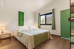 A bedroom with a bed, a nightstand, a green door, and a window with curtains. - Temenino Villa Komako Seaside House (Taiarapu-Ouest)