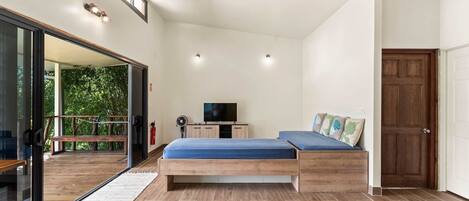 A bedroom with a bed, a TV, a wooden bench, and a view of greenery outside.