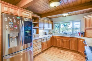 Eine Küche mit Holzausstattung, einem Edelstahlkühlschrank, einer Mikrowelle und einem Fenster mit Blick auf Bäume.
