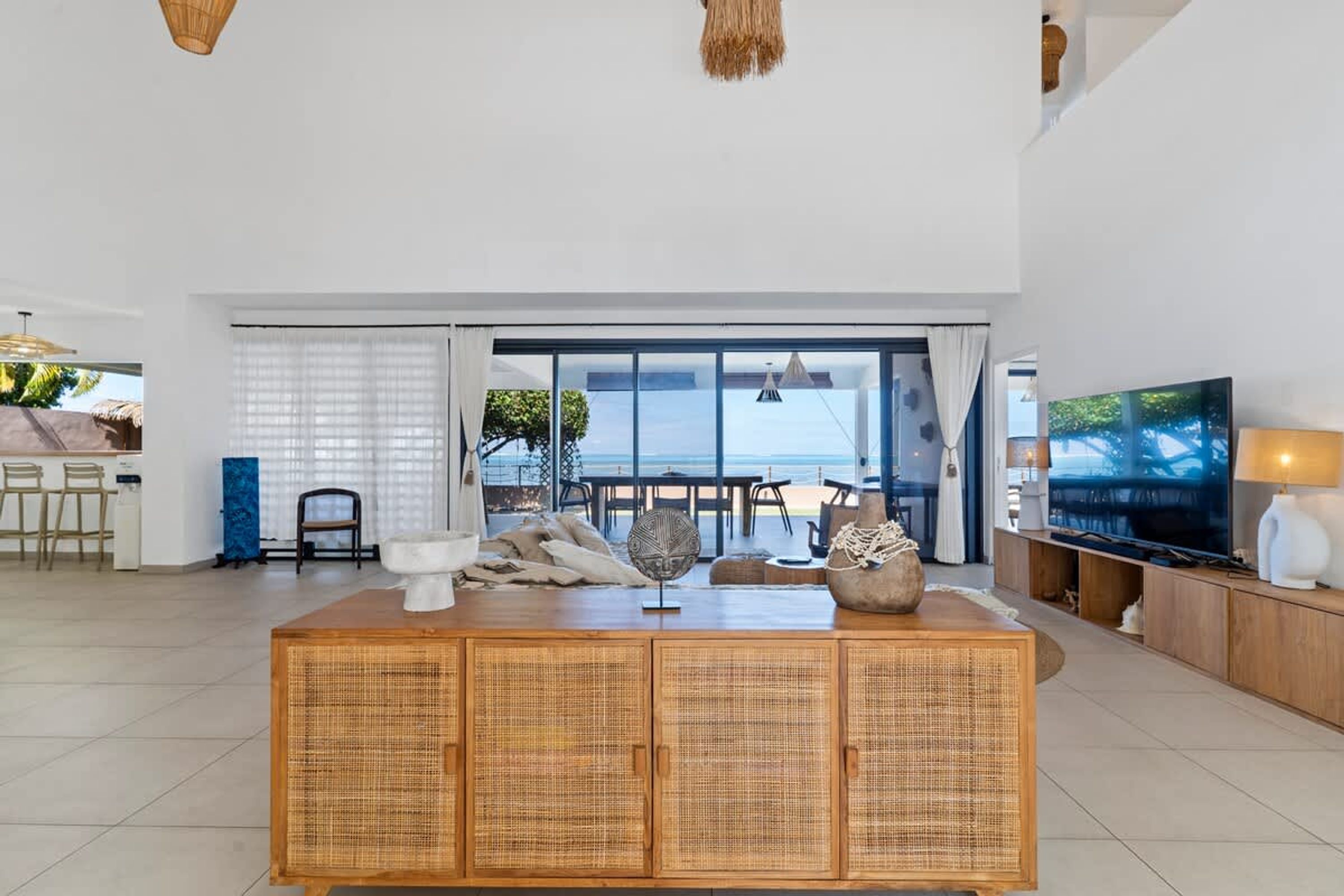 A spacious living area with a large TV, wicker furniture, and a view of the outdoors.