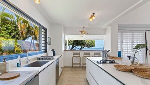Une cuisine moderne dotée d’une grande fenêtre, de tabourets de bar et offrant une vue sur l’océan.