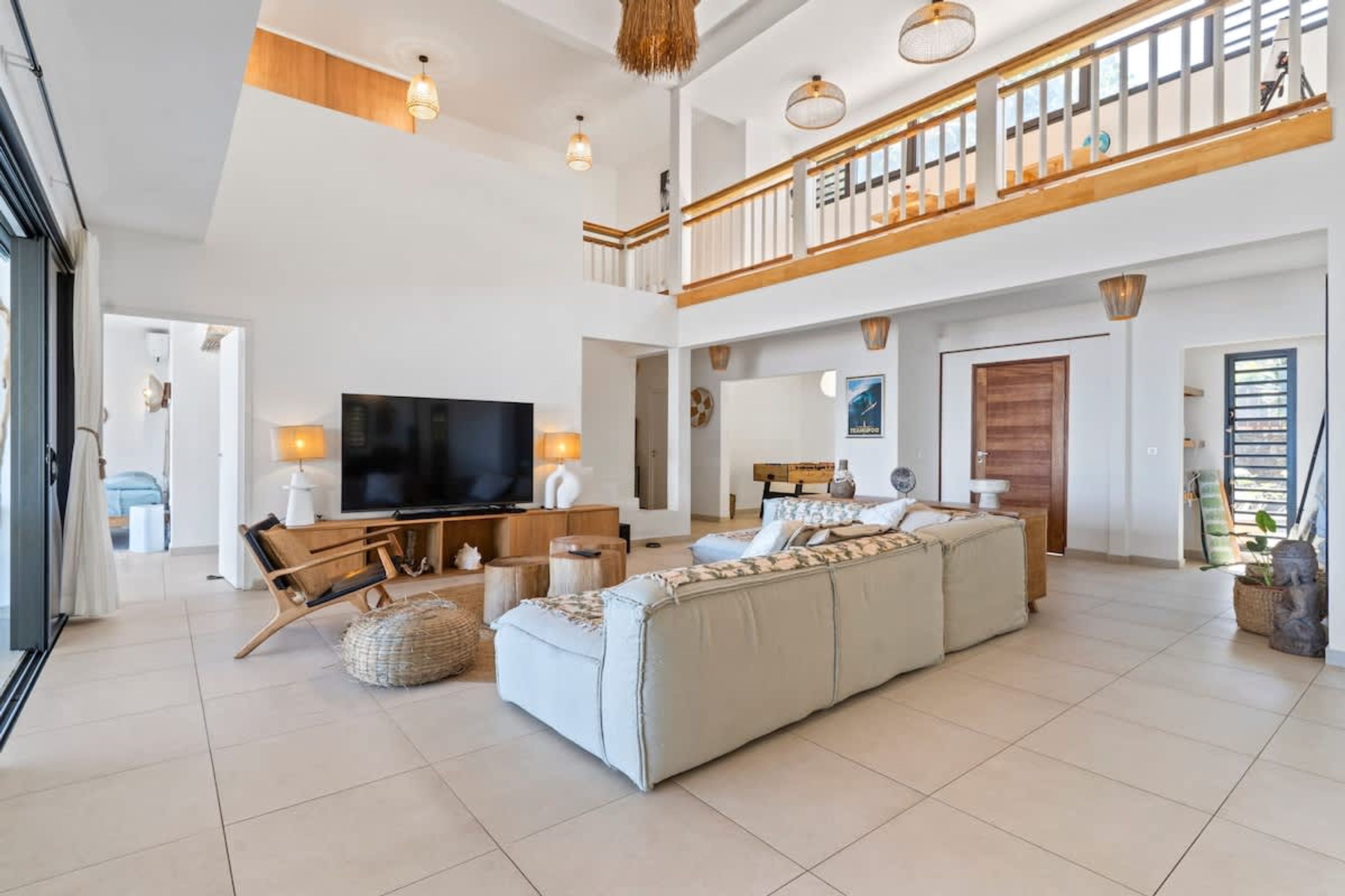Un vaste espace de vie comprenant un grand téléviseur, un canapé, une table basse en bois et un balcon doté d’une balustrade.