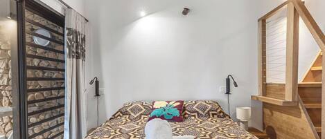 A bedroom with a patterned bedspread, a pair of towels, a wooden staircase, and a stone wall.