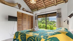 Un dormitorio con cama, televisión, ventilador de techo y vistas a zonas verdes.