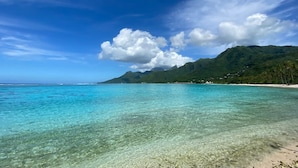A clear view of a beach with turquoise water, a sandy shore, and a mountain in the background. - Seaside Air-conditioned Bungalow Tamara (Moorea-Maiao)