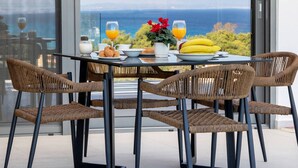 Un tavolo da pranzo con sedie in vimini, un piano in vetro e vista sul mare attraverso ampie finestre.