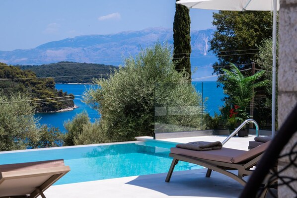 A pool with a view of a body of water and mountains, a lounge chair, and a potted plant. - Villa Unique in Lefkada (Lefkada)