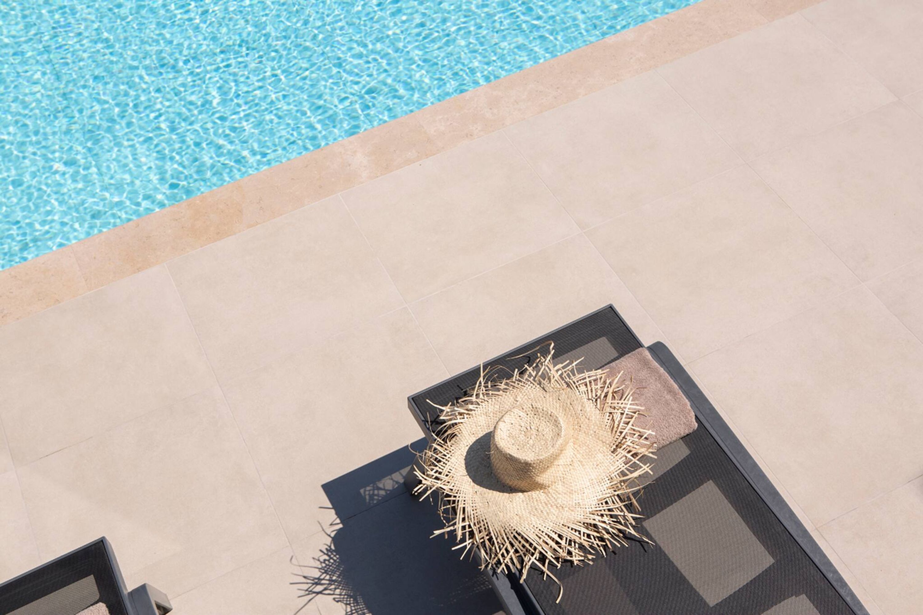 Vista de la piscina con un toldo y un sombrero de paja sobre una mesa.