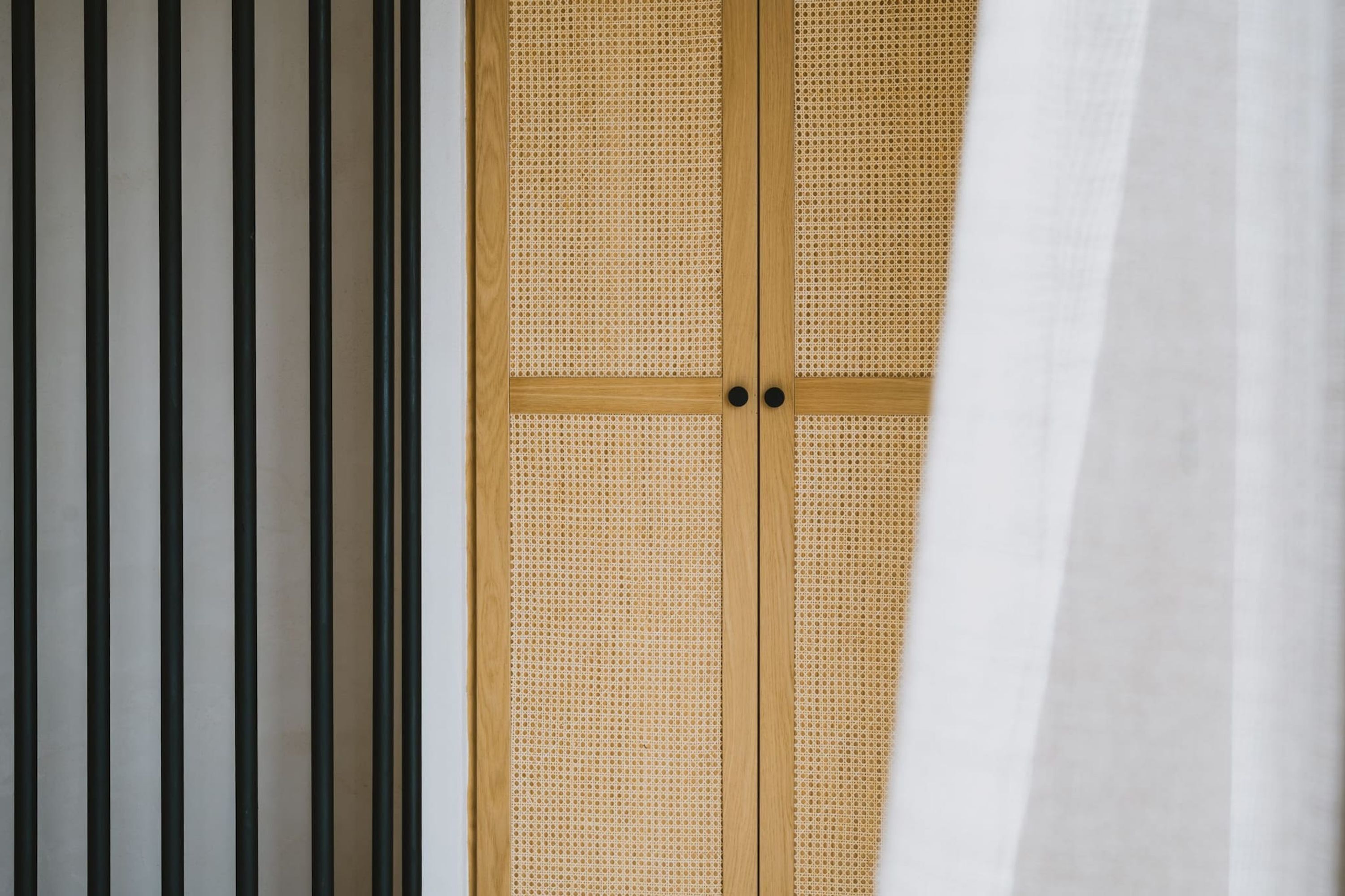 Ein Zimmer mit Holztür, einem schwarz-weißen Streifenmuster an der Wand und einem weißem, halb zurückgezogenen Vorhang.