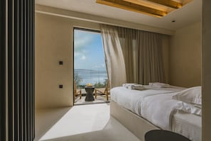 Un dormitorio moderno con un ventanal grande, una cama, una mesita y una silla.