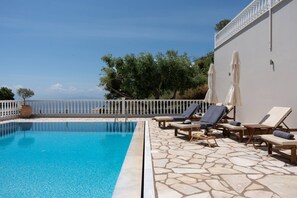 A poolside area with lounge chairs and umbrellas, a stone-tiled floor, and a view of the sea. - Dream 1 BED in Ponti (Lefkada)