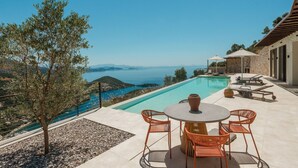 A poolside area with a table and chairs, a view of the sea, and a stone building. - FR Villa Mulberry in Sivota (Lefkada)