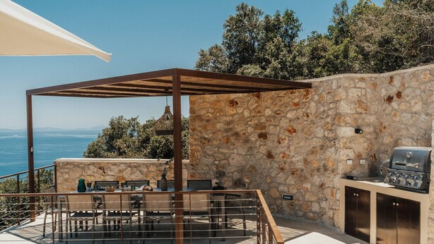 An outdoor patio with a stone wall, a pergola, a grill, and a table with chairs. - FR Villa Mulberry in Sivota (Lefkada)
