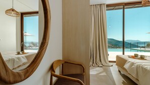A hotel room with a large mirror, a wooden chair, two beds, a view of the mountains, and a balcony with a table and chairs. - FR Villa Mulberry in Sivota (Lefkada)