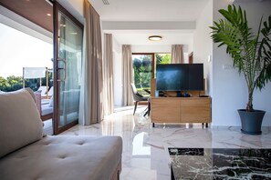 A modern living room with a sofa, a television, a wooden cabinet, and a potted plant. - Zavia Villa Bita 2B Syvota (Igoumenitsa)