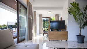 A modern living room with a sofa, a television, a potted plant, and a sliding glass door leading to an outdoor area. - Zavia Villa Alpha 2B Syvota (Igoumenitsa)
