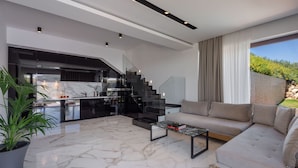 A modern living room with a marble floor, a sofa, a coffee table, and a staircase leading to a kitchen. - Zavia Villa Alpha 2B Syvota (Igoumenitsa)