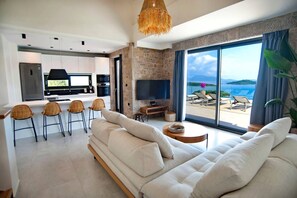 A modern living area with a sofa, chairs, a TV, and a view of the outdoors. - Smirties Villa Haris 2bed (Lefkada)