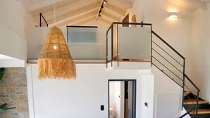 A modern interior with a sofa, a hanging light fixture, a staircase, and a view of a room with a bed. - Smirties Villa Haris 2bed (Lefkada)