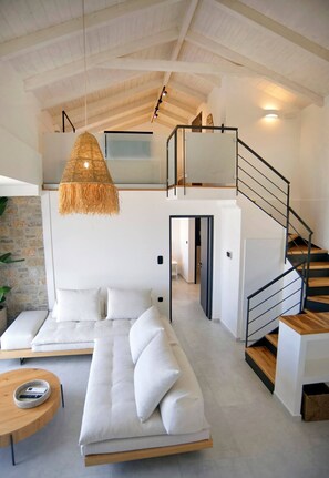A modern interior with a sofa, a hanging light fixture, a staircase, and a view of a room with a bed. - Smirties Villa Haris 2bed (Lefkada)