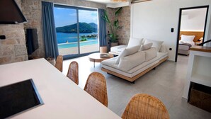 A modern living room with a sofa, dining table, chairs, and a view of the sea. - Smirties Villa Haris 2bed (Lefkada)