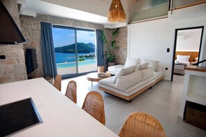 A modern living room with a sofa, dining table, chairs, and a view of the sea. - Smirties Villa Haris 2bed (Lefkada)