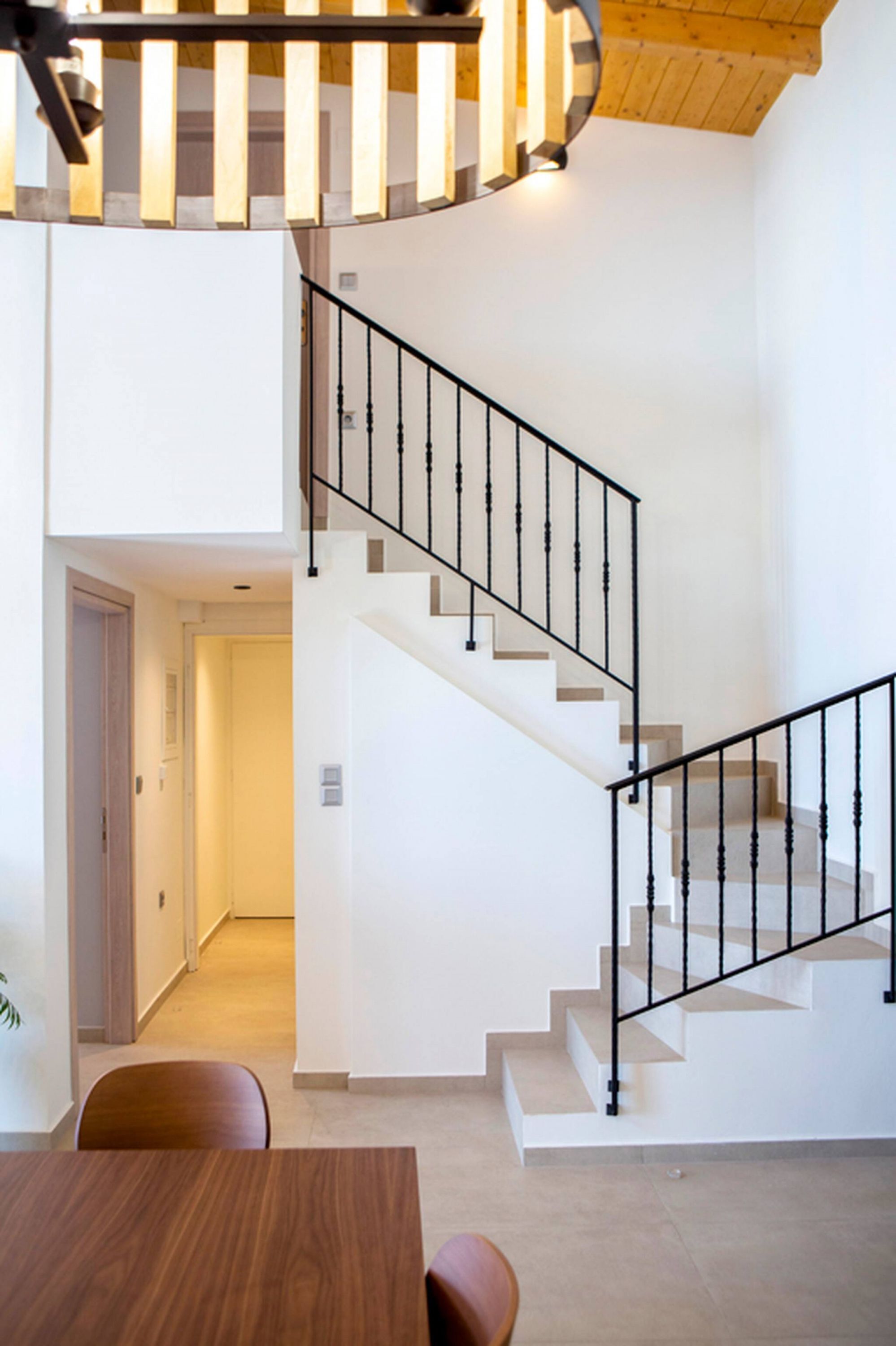 Un intérieur moderne avec un escalier en colimaçon, un coin repas et une porte visible donnant sur une autre pièce.