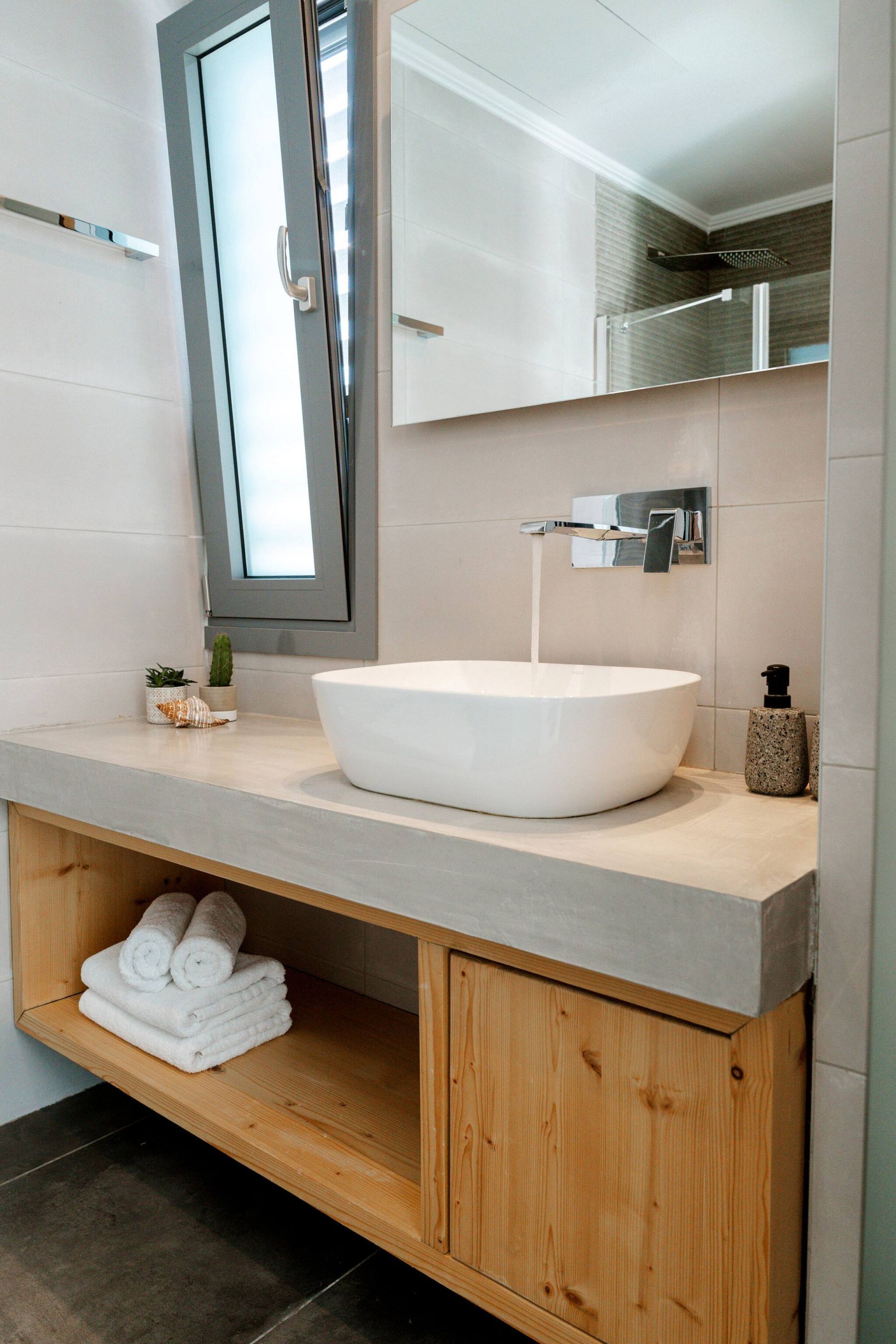 Une salle de bain moderne avec un grand lavabo blanc, un meuble-lavabo en bois, un miroir et une petite plante.