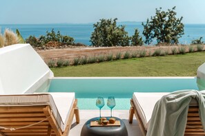 Vista de la piscina con sillones reclinables, una mesa con bebidas y vista al mar.
