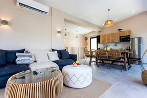 A modern living room with a sofa, ottoman, and coffee table, a dining area with chairs and a table, and a kitchen with wooden cabinets and appliances. - Desimi Villa Luca in Lefkada (Lefkada)