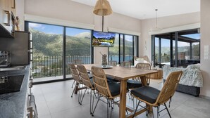 A spacious dining area with a large table and chairs, a television mounted on the wall, and a view of mountains through large windows. - Desimi Villa Luca in Lefkada (Lefkada)