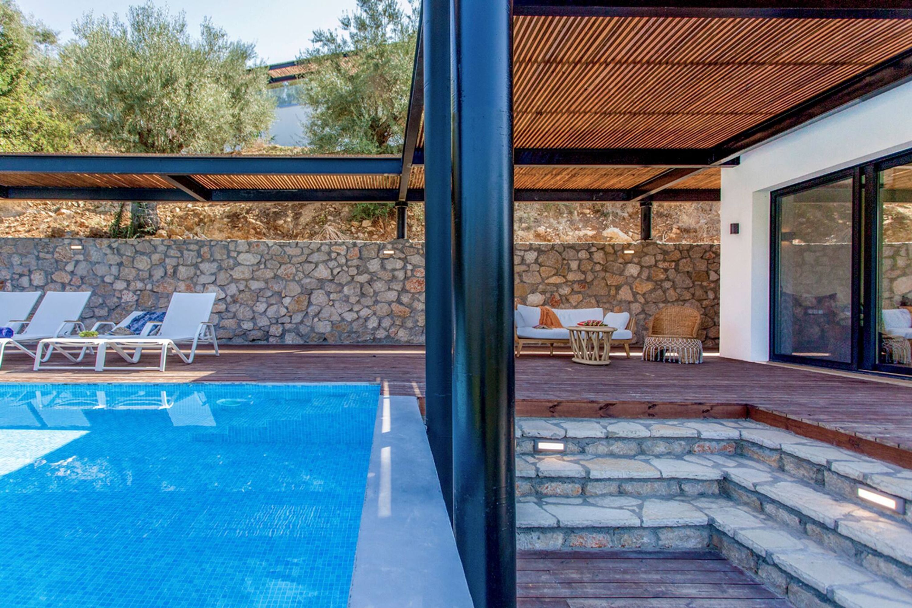 Un espace piscine extérieur moderne, doté de chaises longues, d’un mur en pierre et d’une terrasse en bois.