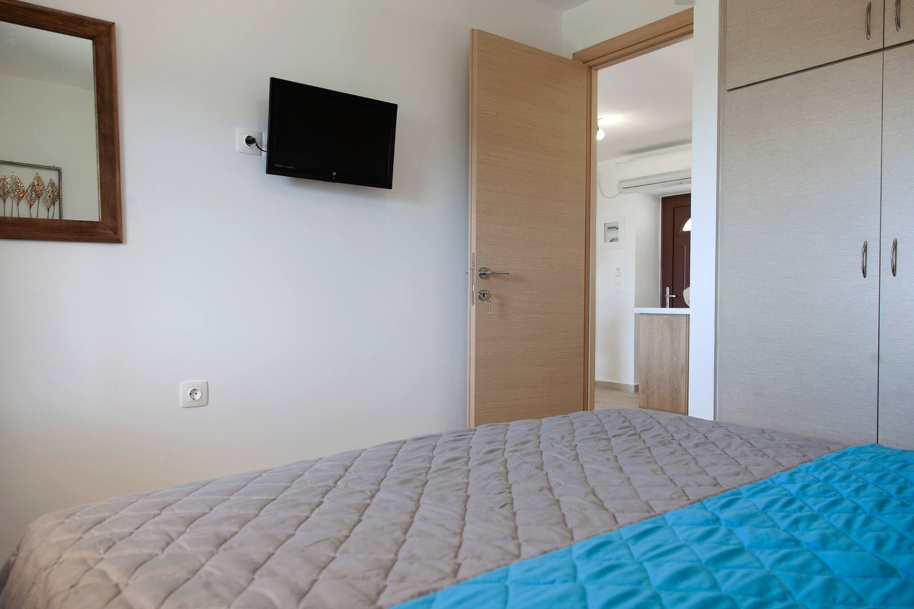 A bedroom with a bed, a television mounted on the wall, and a wardrobe.