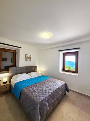 A bedroom with a bed, bedside lamps, a window with a view, and a ceiling light. - Agios Petros 2 in Agios Petros (Lefkada)