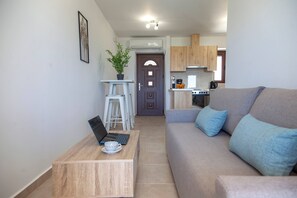 A modern living room with a sofa, a small table with a laptop, and a staircase leading to a kitchen. - Agios Petros 2 in Agios Petros (Lefkada)