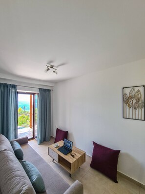 A modern living room with a sofa, a wooden coffee table with a laptop, and a view through a glass door. - Agios Petros 2 in Agios Petros (Lefkada)