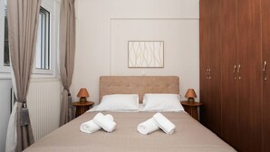 Ett hotellrum med en säng, två sänglampor, ett fönster med gardiner, ett element och en garderob i trä.
