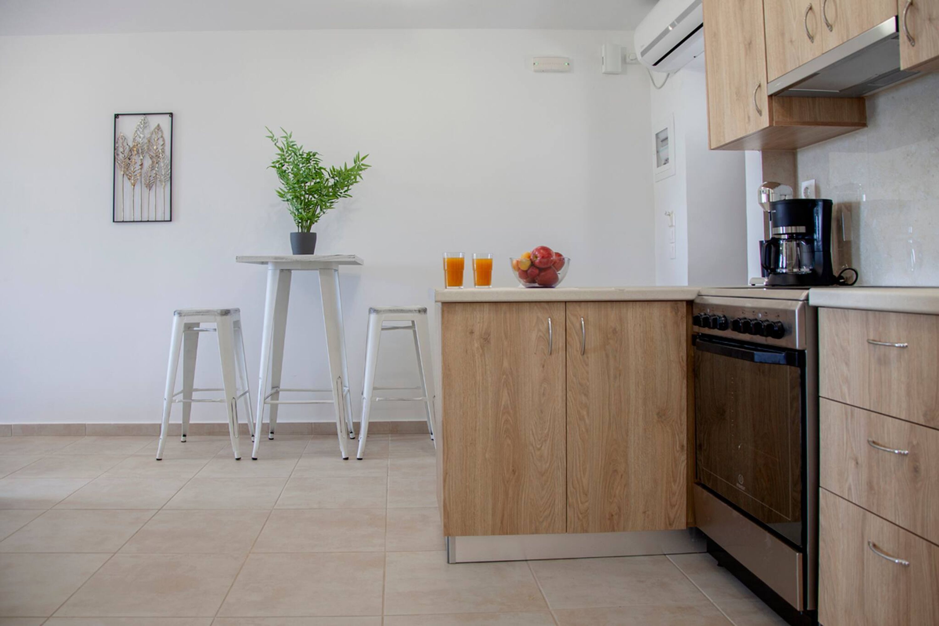 Une cuisine avec des meubles de rangement en bois, un four en acier inoxydable, une machine à café et une petite table avec des tabourets.