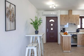 A modern kitchen with a central island, a dining area with stools, a potted plant, and a framed artwork on the wall.
