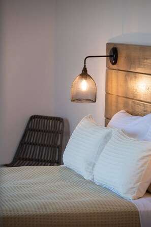 Ein Bett mit weißer Bettwäsche, einem strukturierten Kopfteil und einer Wandlampe.