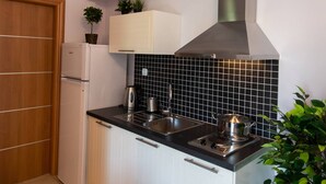 A modern kitchen with white cabinets, a black tiled backsplash, a stainless steel range hood, and a built-in sink. - Drakatos K Apartment (Lefkada)