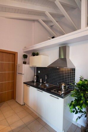 A modern kitchen with white cabinets, a black tiled backsplash, a stainless steel range hood, and a built-in sink. - Drakatos K Apartment (Lefkada)