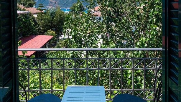 A balcony with a table and two chairs, overlooking a mountainous landscape with trees and buildings. - Drakatos K Apartment (Lefkada)