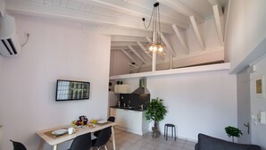 A modern kitchen with a dining area, a black sofa, and a staircase leading to an upper level. - Drakatos K Apartment (Lefkada)
