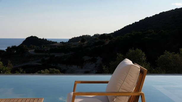 A wooden chair with a cushion by an infinity pool overlooking a coastal landscape. - Scirocco Telemachos 1 BED (Lefkada)